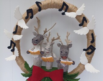 May include: A felt Christmas wreath with three reindeer singing carols. The wreath is decorated with white felt wings and black musical notes. The reindeer are holding sheet music and are wearing red bows.