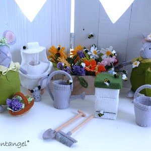 In this picture: two handmade felt mice, dressed as a garden lady and garderer, with planting pot with flowers, beehive and beekeeper set, bucket, spade, rake and watering can. All made with a PDF handsewing pattern from WoolFeltwonders and this pattern is part of a series with felt toy aniamals and costume patterns to mix and match and to portray hobby or professon, for decoration and play.
