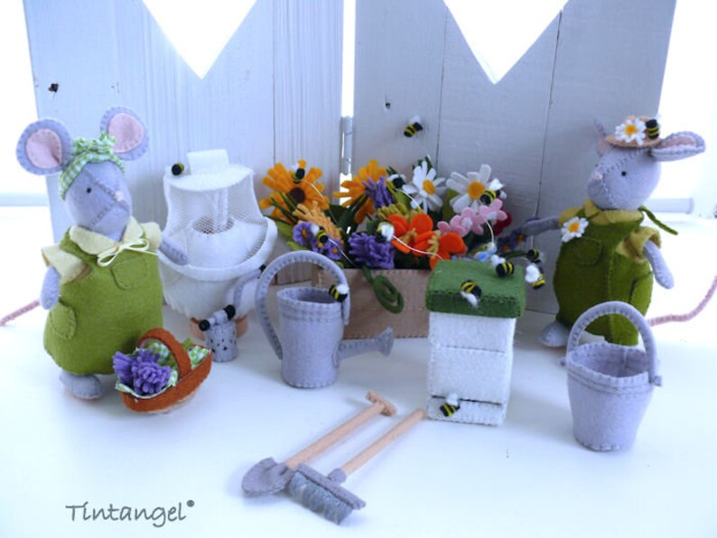In this picture: two handmade felt mice, dressed as a garden lady and garderer, with planting pot with flowers, beehive and beekeeper set, bucket, spade, rake and watering can. All made with a PDF handsewing pattern from WoolFeltwonders and this pattern is part of a series with felt toy aniamals and costume patterns to mix and match and to portray hobby or professon, for decoration and play.