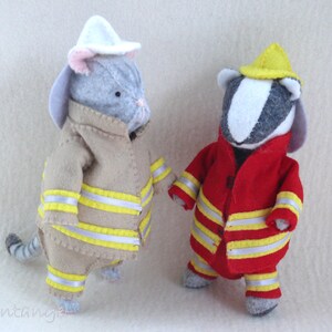 In this picture: two handmade felt toy animals, cat and badger, both dressed as a firefighter, one in a red costume, the other in a sand-colored costume. All clothing has refelcting stripes in yellow and silver. The badger with the red costume wears a yellow helmet, the other has a white helmet. All is made with a PDF handsewing pattern from WoolFeltWonders, part of a series with toy animal and clothing patterns to mix and match, to portray hobby or profession for play.