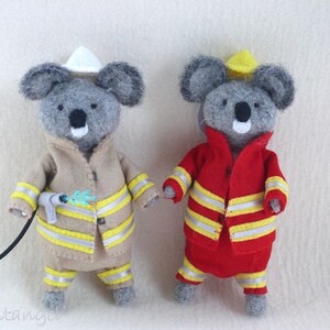In this picture: two handmade felt koala bears, both dressed as a firefighter, one in a red costume, the other in a sand-colored costume. all clothing has refelcting stripes in yellow and silver. The koala bear with the sand- colored costume wears a white helmet and holds the waterhose, the other has a yellow helmet. All is made with a PDF handsewing pattern from WoolFeltWonders, part of a series with toy animal and clothing patterns to mix and match, to portray hobby or profession for play.