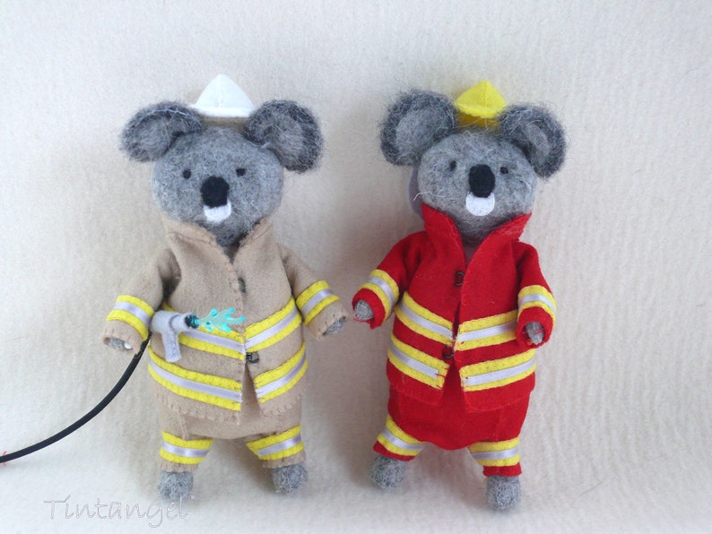 In this picture: two handmade felt koala bears, both dressed as a firefighter, one in a red costume, the other in a sand-colored costume. all clothing has refelcting stripes in yellow and silver. The koala bear with the sand- colored costume wears a white helmet and holds the waterhose, the other has a yellow helmet. All is made with a PDF handsewing pattern from WoolFeltWonders, part of a series with toy animal and clothing patterns to mix and match, to portray hobby or profession for play.