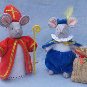 May include: Two felt mouse figurines dressed as Saint Nicholas and a page. The Saint Nicholas mouse is wearing a red robe with gold trim and a mitre. The page mouse is wearing a blue and white costume with a yellow feather.