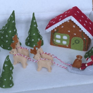 May include: A felt Christmas scene with a gingerbread house, a red-suited Santa Claus in a sleigh pulled by four reindeer, and several green trees with white snowflakes.