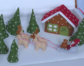 May include: A felt Christmas scene with a gingerbread house, a red-suited Santa Claus in a sleigh pulled by four reindeer, and several green trees with white snowflakes.