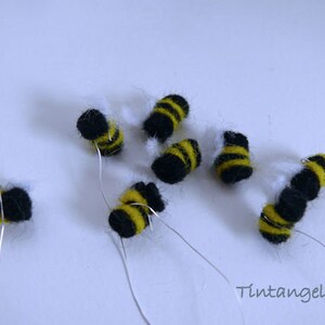 in this picture: 8 handmade felt bees, black with yellow stripes and white wings, all on a piece of thin silver wire. Thess bees are aprt of a PDF handsewing pattern from WoolFeltwonders to dress a felt toy animal as a bee keeper. the set contains, the clothing, bee hood, beehive, smoke pipe and these bees. Part of a series with felt toy animals and all kinds of clothing sets to mix and match to portray hobby or profession. Easy to make animals and clothing sets for decoration and play