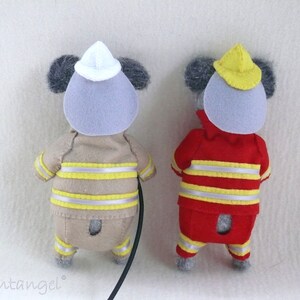 In this picture: two handmade felt koala bears, both dressed as a firefighter, one in a red costume, the other in a sand-colored costume. all clothing has refelcting stripes in yellow and silver. The koala bear with the sand- colored costume wears a white helmet and holds the waterhose, the other has a yellow helmet. All is made with a PDF handsewing pattern from WoolFeltWonders, part of a series with toy animal and clothing patterns to mix and match, to portray hobby or profession for play.