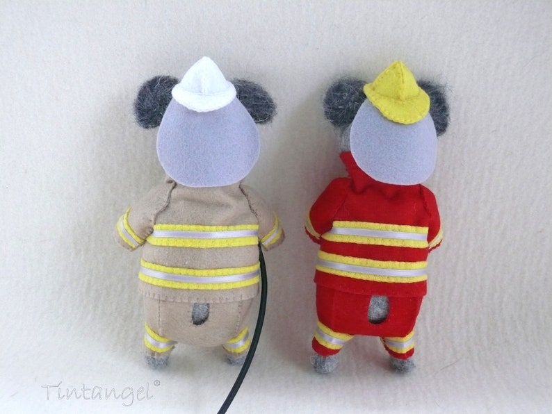 In this picture: two handmade felt koala bears, both dressed as a firefighter, one in a red costume, the other in a sand-colored costume. all clothing has refelcting stripes in yellow and silver. The koala bear with the sand- colored costume wears a white helmet and holds the waterhose, the other has a yellow helmet. All is made with a PDF handsewing pattern from WoolFeltWonders, part of a series with toy animal and clothing patterns to mix and match, to portray hobby or profession for play.
