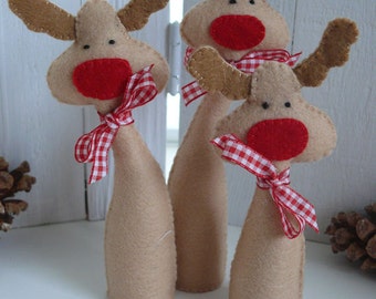 May include: Three brown felt reindeer ornaments with red felt noses and white and red gingham ribbon bows. The reindeer are standing on a white surface.