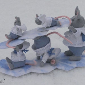 Può includere: Quattro figurine di topo in feltro sono su mini snowboard. I topi indossano abiti blu e bianchi e hanno il naso rosa. Gli snowboard sono bianchi con accenti blu. I topi sono su uno sfondo bianco.