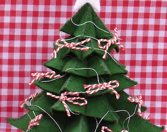 Könnte beinhalten: Ein grüner Filz-Weihnachtsbaum mit einem weißen Stern oben und roten und weißen Schleifen aus Schnur als Dekoration. Der Baum steht auf einer rot-weiß karierten Tischdecke.