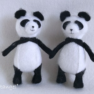 May include: Two black and white panda bear plush toys with black eyes and noses. The pandas are holding hands and standing on a white surface.