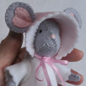 In this picture: a detail of  a mouse, dressed in a pink dress with white cape, white and pink bonnet. Made with a PDF hand sewing pattern from WoolFeltwonders by Tintangel.