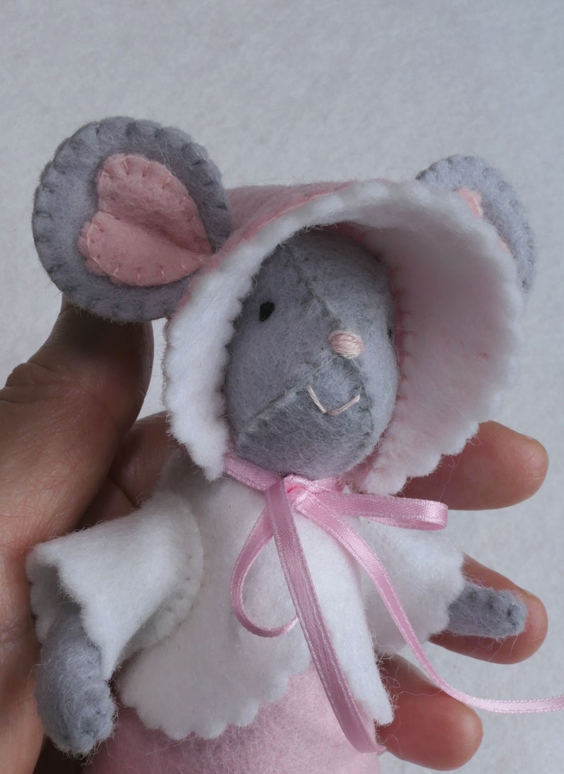 In this picture: a detail of  a mouse, dressed in a pink dress with white cape, white and pink bonnet. Made with a PDF hand sewing pattern from WoolFeltwonders by Tintangel.