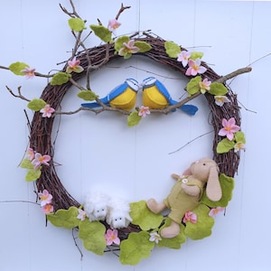 May include: A brown twig wreath decorated with felt bluebirds, white lambs, and pink felt flowers.