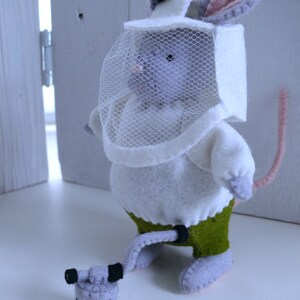 In this picture: a handmade felt mouse dressed as a beekeeper, with white jacket, bee hood, and smoke pipe. All this is is made with PDF hand sewing pattern from WoolFeltWonders by Tintangel and is part of a series with felt toy animals and all kinds of clothing sets to mix and match to portray hobby or profession. Easy to make animals and clothing sets for decoration and play.