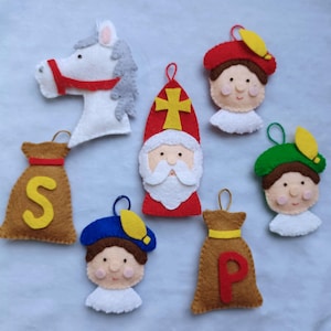 Op de afbeelding: Vilt ornamenten die Sinterklaas en zijn helpers voorstellen. De ornamenten omvatten een wit paard, een rood geklede Sinterklaas met een witte baard, een bruine zak met de letter 'S', een helper met een blauwe hoed, een bruine zak met de letter 'P' en een helper met een groene hoed.