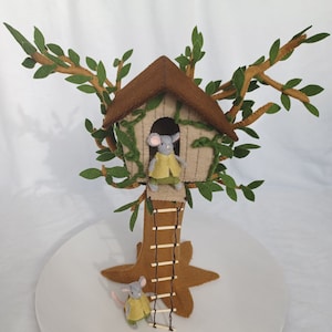 May include: A felt treehouse with a brown roof and green leaves. Two small gray mice with yellow shirts are climbing the ladder to the treehouse.