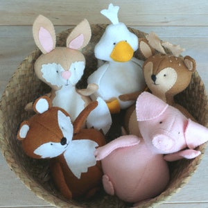 May include: A wicker basket filled with five felt animal toys: a brown rabbit, a brown fox, a white duck, a brown deer, and a pink pig.
