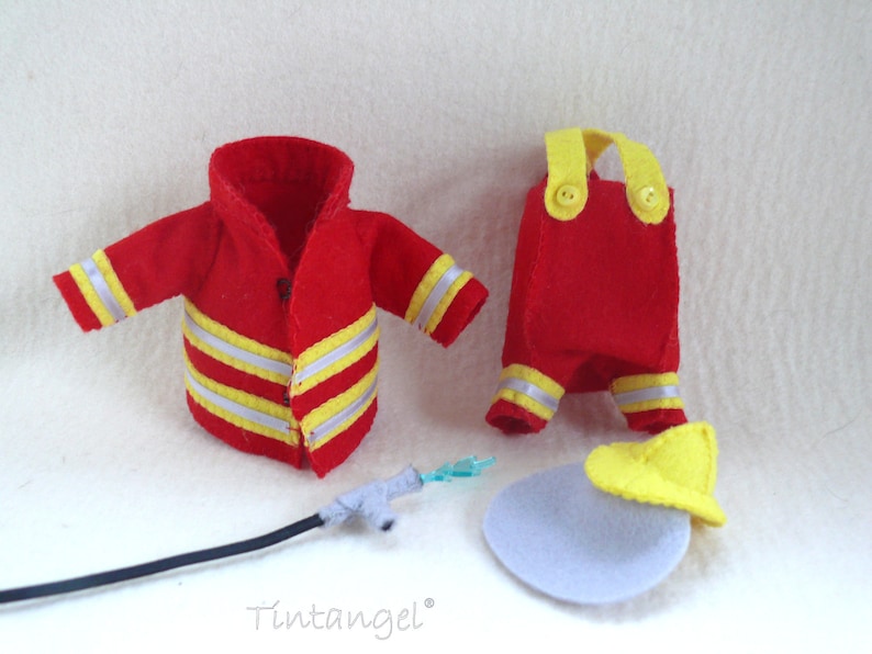 In this picture: a firefigther costumes for felt toy animals, made with a PDF handsewing pattern from WoolFeltWonders, part of a series with toy animal and clothing patterns to mix and match, to portray hobby or profession, for decoration and play. this set has a red jacket and trousers with yellow helmet.  All clothes have reflecting stripes in yellow and silver. A waterhose is lying in front of the clothes.
