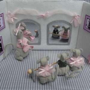 Pode incluir: Um cenário de teatro de feltro com ratos cinzentos vestidos com tutus e laços cor-de-rosa. O cenário tem duas janelas arqueadas com interiores espelhados e quadros emoldurados. O fundo é branco com detalhes cor-de-rosa.