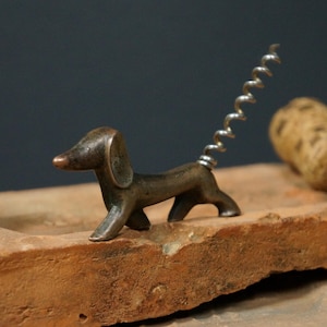 Könnte beinhalten: Ein Flaschenöffner aus Bronze in Form eines Dackels mit einem silbernen Korkenzieher-Schwanz.