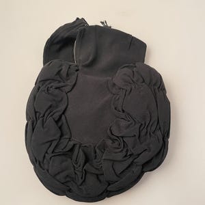 May include: Black, gathered fabric clutch with a rounded shape. The clutch features a ruched design around the edges and a structured top with a small handle. The fabric appears to be a ribbed material.
