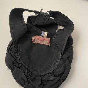 May include: A black hat with a unique design, featuring a rounded crown and a structured brim. The hat has a label that reads "CIANRIDGE". The hat's design includes a series of gathered fabric details, adding texture and visual interest. The hat is made of a dark fabric.