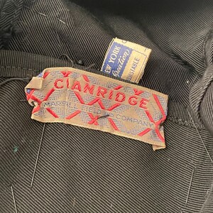 May include: Close-up of a black garment with visible stitching. A label with the text "CIANRIDGE" in red lettering is attached. A smaller tag reads "NEW YORK Creation Adjustable".