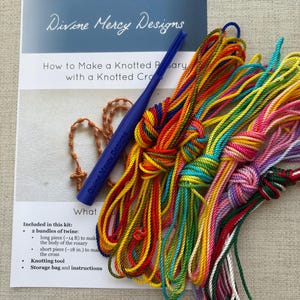 May include: A kit for making a knotted rosary with a knotted cross. The kit includes two bundles of twine, a knotting tool, and instructions. The twine is in a variety of colors, including red, orange, yellow, green, blue, and purple.