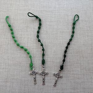 May include: Three green knotted rosary bracelets with silver cross charms.