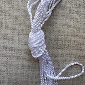 K&ouml;nnte beinhalten: Ein wei&szlig;es Seil ist aufgerollt und zu einem Knoten gebunden. Das Seil besteht aus einem weichen, geflochtenen Material.