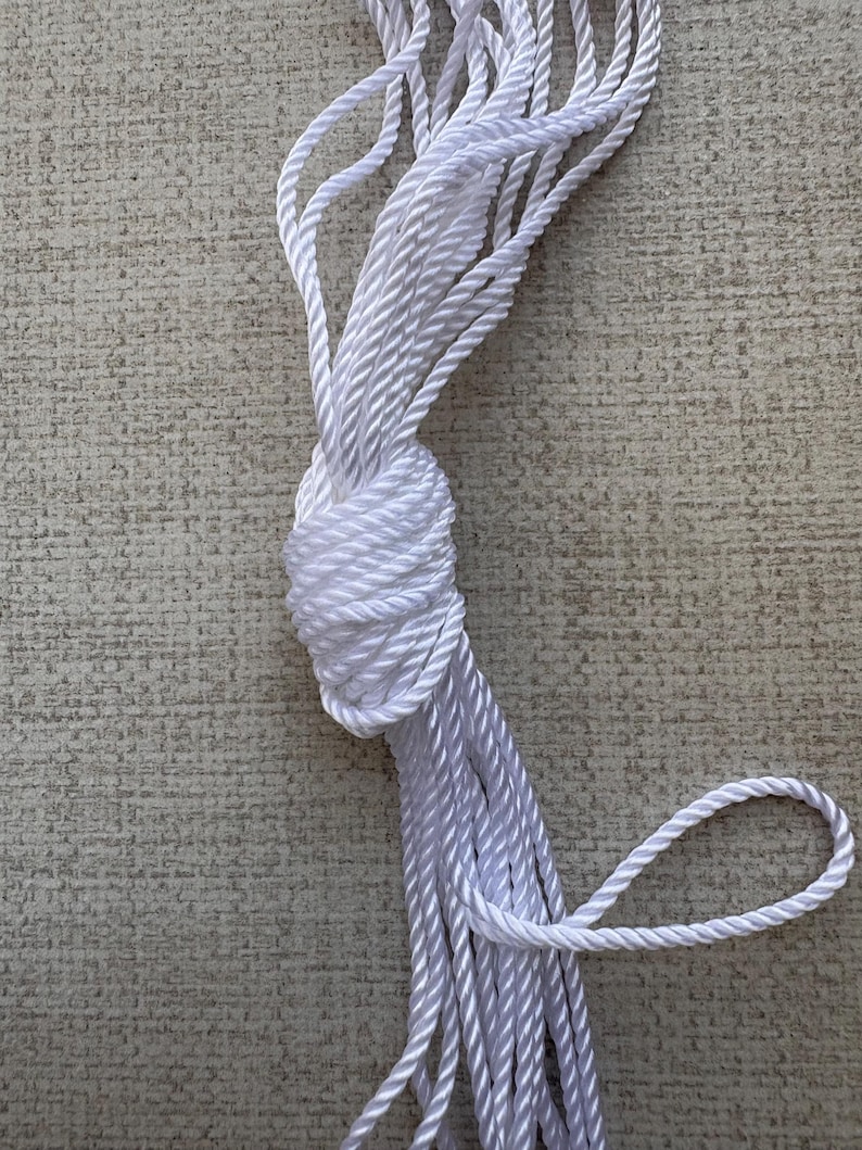 K&ouml;nnte beinhalten: Ein wei&szlig;es Seil ist aufgerollt und zu einem Knoten gebunden. Das Seil besteht aus einem weichen, geflochtenen Material.