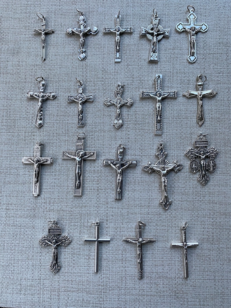 K&ouml;nnte beinhalten: Eine Sammlung von 19 silberfarbenen Kreuzanh&auml;ngern mit verschiedenen Designs, darunter einfache Kreuze, Kreuze mit Figuren und verzierte Kreuze.