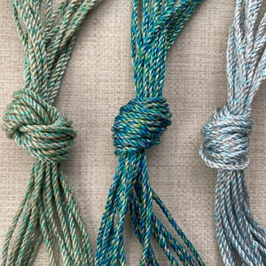 May include: Three spools of twisted cord in different color combinations. The cords are green and gold, blue and gold, and light blue and silver.