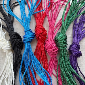 May include: A collection of seven different coloured ropes, each tied in a knot. The ropes are white, black, blue, red, pink, green, and purple.
