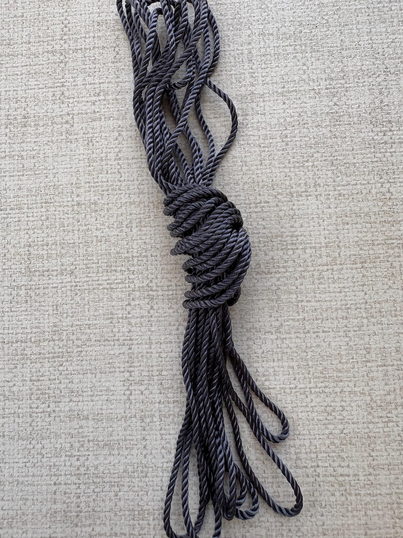 K&ouml;nnte beinhalten: Ein langes St&uuml;ck schwarzes geflochtenes Seil, aufgerollt und zu einem Knoten gebunden.