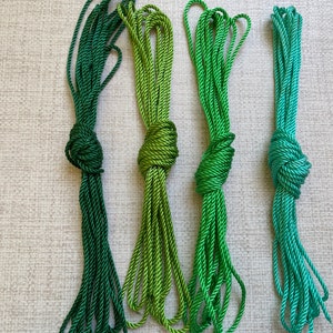 May include: Four spools of green cord, each a different shade of green, from dark green to light green. The cords are tied in knots.