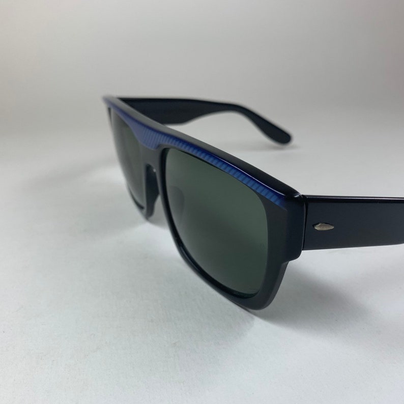 Peut inclure: Lunettes de soleil noires avec une bordure bleue sur la monture. Les verres sont vert fonc&eacute;.