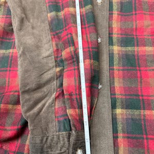 以下が含まれることがあります： 赤と緑の格子柄のフランネルシャツ。左袖に茶色のスエードパッチ、カフスはコーデュロイ。ボタン留め、標準的な襟です。