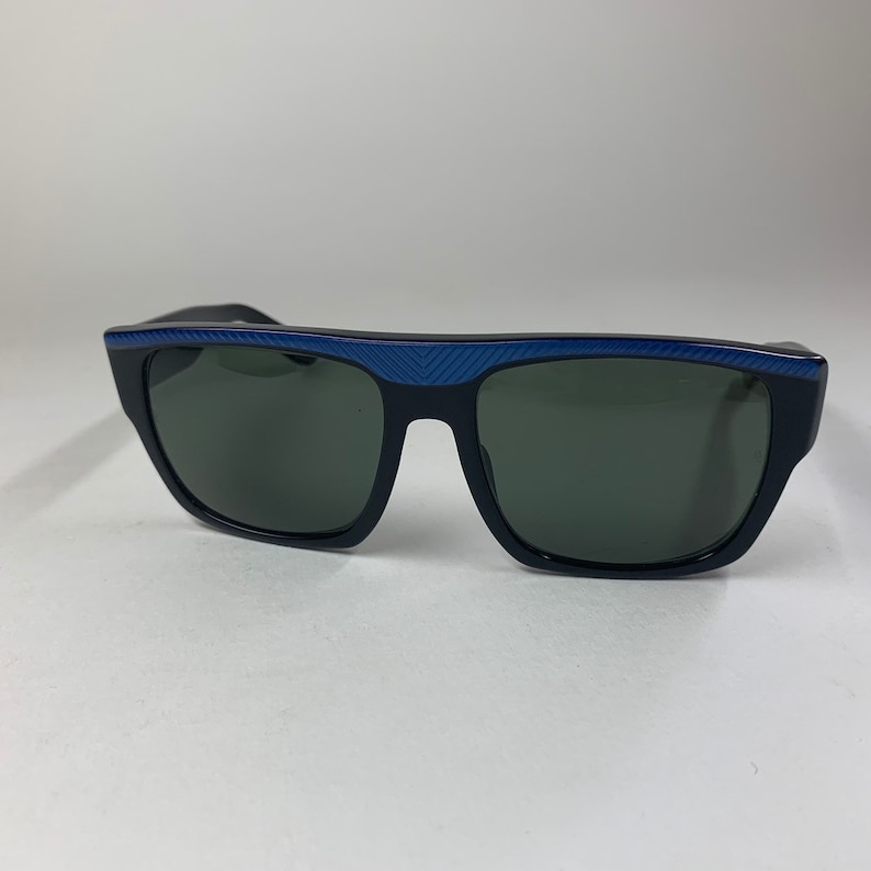 Peut inclure: Lunettes de soleil noires avec une bordure bleue sur la monture. Les verres sont vert fonc&eacute;.