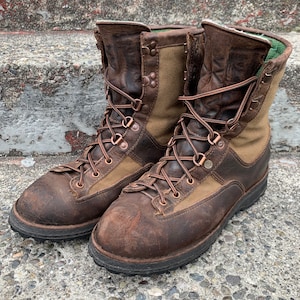May include: A pair of brown leather hiking boots with tan canvas accents and copper eyelets. The boots have a rugged look and are laced up.