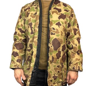 May include: A camouflage print jacket with a black zip and a large pocket on the front.