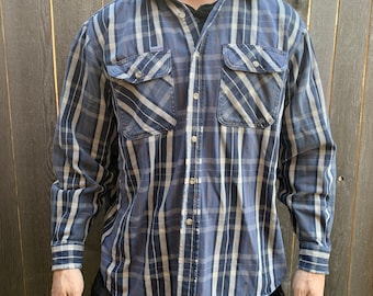 Può includere: Una camicia a maniche lunghe a quadri blu e bianchi con bottoni e due tasche sul petto.