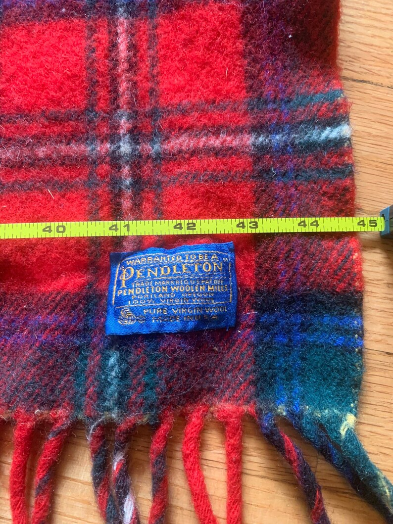 Op de afbeelding: Rode en groene geruite Pendleton wollen sjaal met franjes. Het label luidt "Warranted to be a Pendleton Trade Mark Registered U.S. Pat. Off. Pendleton Woolen Mills Portland, Oregon 100% Virgin Wool Pure Virgin Wool Made in U.S.A."