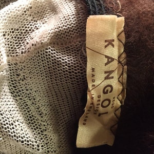 May include: A brown fur coat with a white mesh lining and a brown leather label that reads "Kangol Rego Design Made in England".