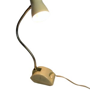 May include: A white desk lamp with a flexible gooseneck arm and a white plastic base. The lamp has a white shade and a light bulb that is turned on.