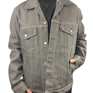 May include: A gray denim jacket with a button closure and a red tab on the pocket.