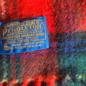 Op de afbeelding: Een blauw label met witte tekst die "WARRANTED TO BE A PENDLETON" en "TRADE MARK REG US PAT OFF PENDLETON WOOLEN MILLS PORTLAND OREGON 100% VIRGIN WOOL PURE VIRGIN WOOL MADE IN USA." zegt.
