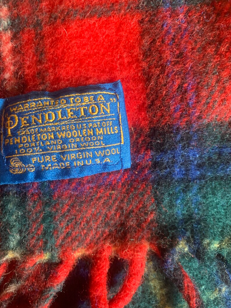 Op de afbeelding: Een blauw label met witte tekst die "WARRANTED TO BE A PENDLETON" en "TRADE MARK REG US PAT OFF PENDLETON WOOLEN MILLS PORTLAND OREGON 100% VIRGIN WOOL PURE VIRGIN WOOL MADE IN USA." zegt.